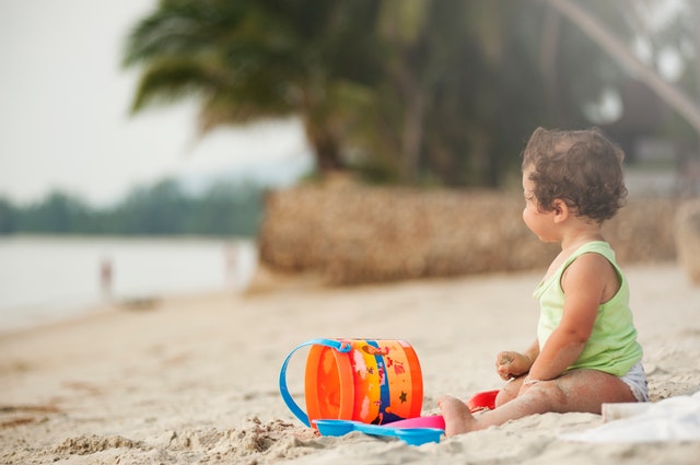 Malý chlapček sedí na pláži a hrá sa s plastovým vedierkom.jpg